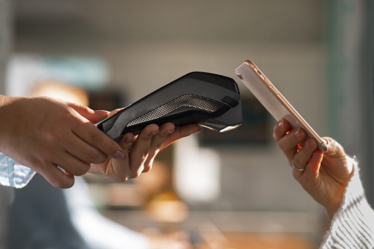 Jongere rekent contactloos af met een smartphone bij een betaalautomaat in een winkel of horecagelegenheid.