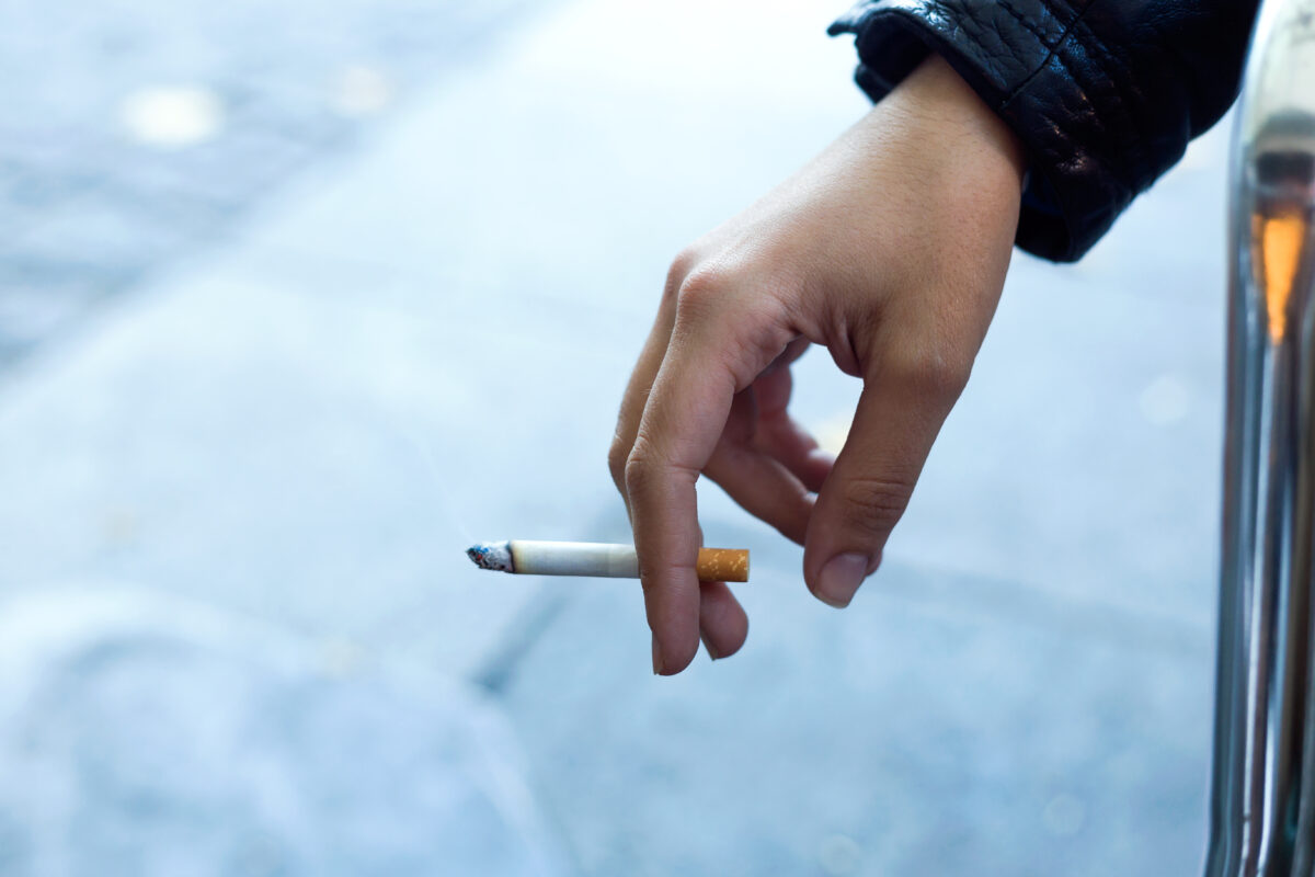 Jongere houdt buiten een brandende sigaret vast, symbool voor roken, meeroken en de invloed van tabaksgebruik op jongeren.