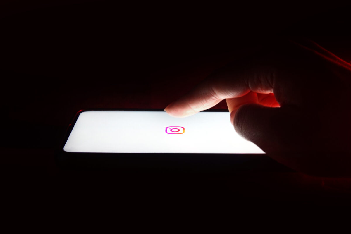 Hand die een smartphone met het Instagram-logo vasthoudt, symbool voor burner accounts en anoniem gebruik van sociale media.