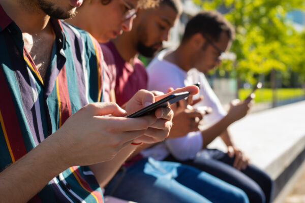 Jongeren zitten naast elkaar op een bankje en kijken geconcentreerd op hun smartphone. De afbeelding illustreert hoe sociale media en privécommunicatie een belangrijk onderdeel zijn van het dagelijks leven.