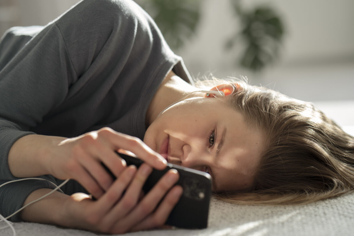 Jongere ligt op bed en kijkt somber naar een smartphone, als illustratie van de invloed van sociale media op de mentale gezondheid.
