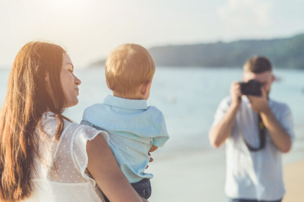 Ouders maken tijdens een strandvakantie een foto van hun jonge kind, als voorbeeld van sharenting en het delen van gezinsfoto's op sociale media.