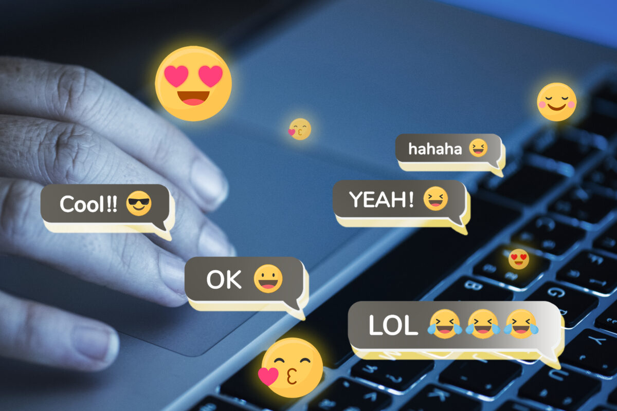 Hand op een laptoptoetsenbord met zwevende emoji’s en online reacties, als illustratie van engagement en rage bait op sociale media.