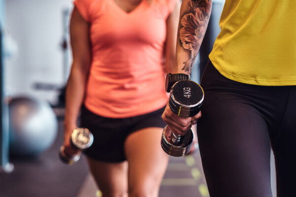 Twee sportende vrouwen trainen met dumbbells in een sportschool.
