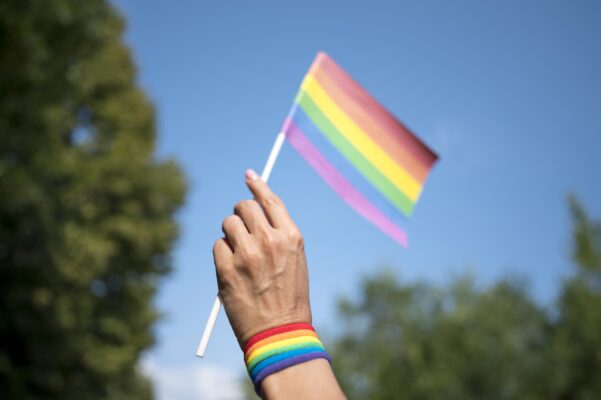Hand houdt een regenboogvlag vast tegen een blauwe lucht, passend bij het onderwerp homo-acceptatie onder jongeren.