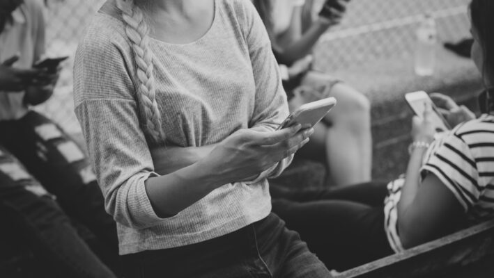 Jongeren zitten samen buiten en gebruiken hun smartphone, passend bij online gesprekken over therapy speak en relaties.