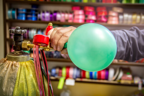 Persoon vult een ballon met lachgas vanuit een grote gascilinder, een veelgebruikte manier waarop lachgas recreatief wordt gebruikt.
