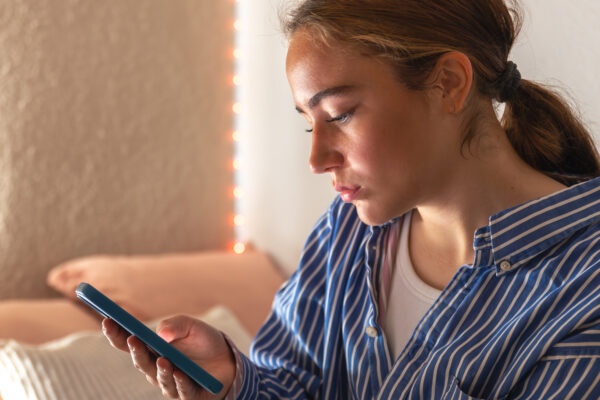 Jongere kijkt naar haar smartphone en zoekt mogelijk informatie over ADHD, autisme of trauma via sociale media.